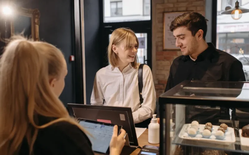 Operador de caixa sorrindo enquanto atende um cliente em um ambiente de loja moderna, com um terminal de pagamento digital