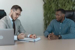 Mulher sorridente em uma entrevista de emprego, com o entrevistador fazendo anotações em um ambiente profissional.
