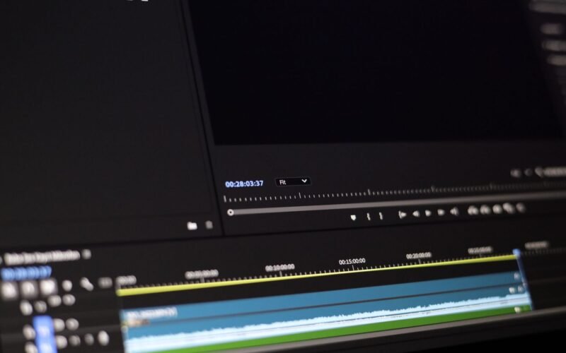 Jovem editor de vídeo freelancer trabalhando em seu laptop, com fones de ouvido e uma interface de software de edição de vídeo na tela, simbolizando trabalho remoto e criatividade.
