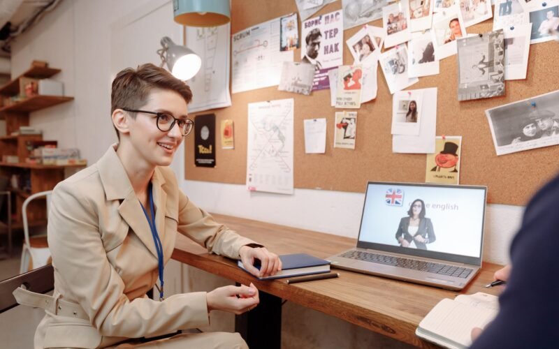 Pessoa sorrindo e usando fones de ouvido em frente a um laptop, simbolizando aprendizado de inglês para aprimoramento profissional.