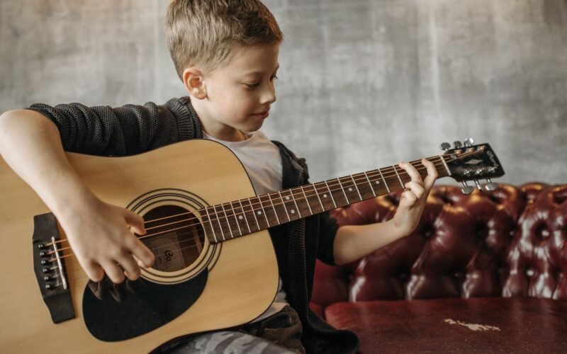 Pessoa tocando violão com partituras e um metrônomo ao lado, simbolizando o aprendizado.