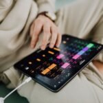 Músico tocando violão em palco, com um tablet em um suporte exibindo cifras em rolagem automática e um pedal bluetooth no chão.