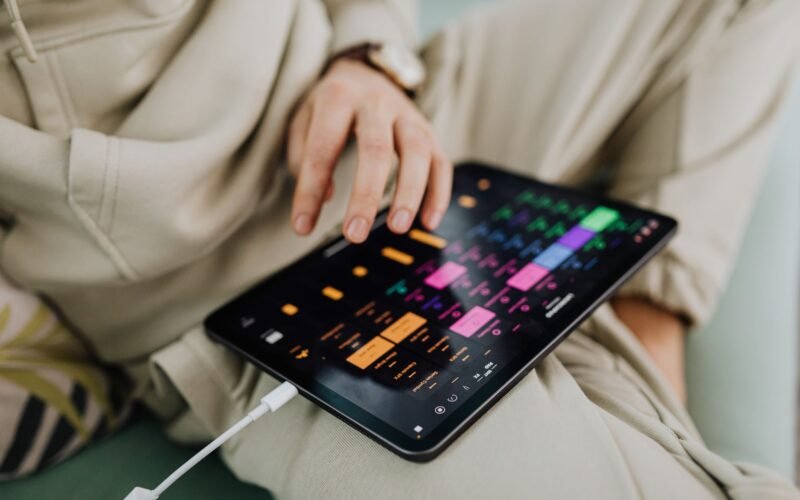 Músico tocando violão em palco, com um tablet em um suporte exibindo cifras em rolagem automática e um pedal bluetooth no chão.