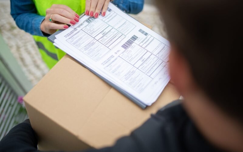 Pessoa analisando documentos de segurança do trabalho em um escritório, com logo da NR1 ao fundo e equipe de segurança.