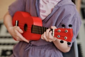 Mãos de um iniciante segurando um cavaquinho e tocando os primeiros acordes, com partituras ao fundo.